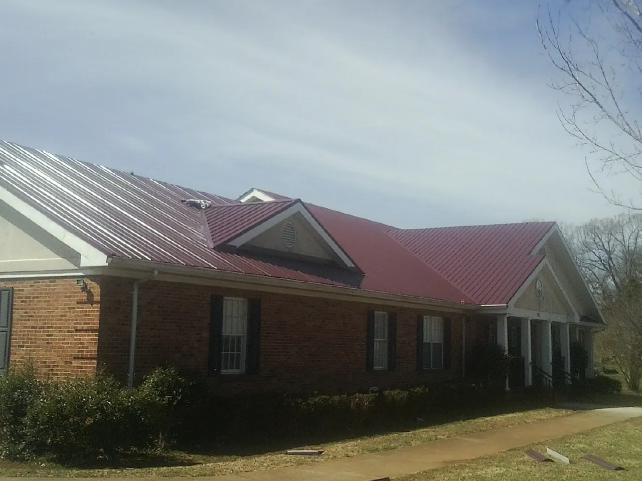 Red metal roof with gabled entries on a long brick building, from a Hail Damage Roof Repair job in De Witt