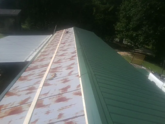 Old rusted panels beside newly installed green metal roofing — Wind Damage Roof Repair by Roofing Brothers in De Witt