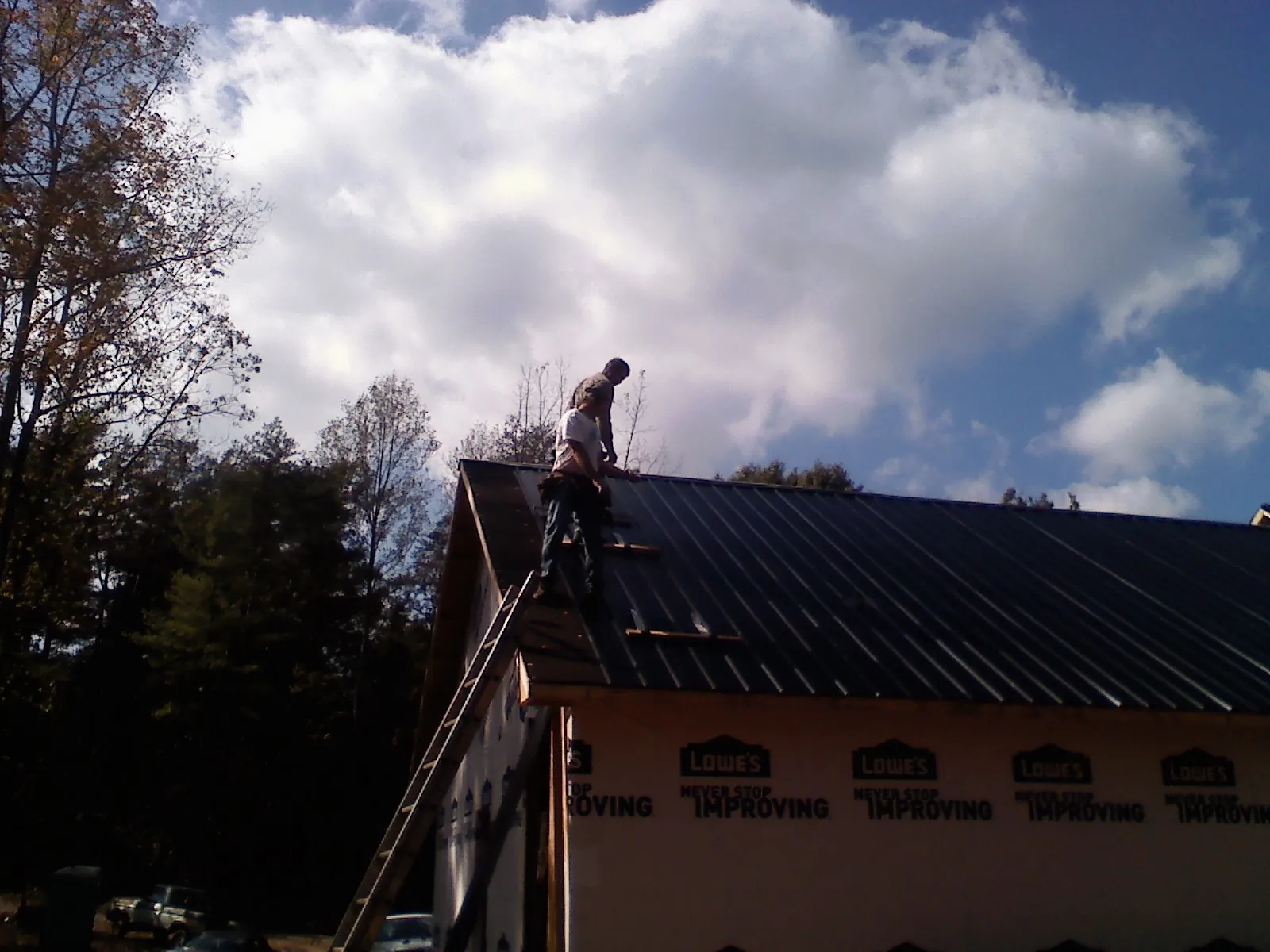 Roofer fastening dark metal panels high against a cloudy sky, from a Roof Inspection job in De Witt