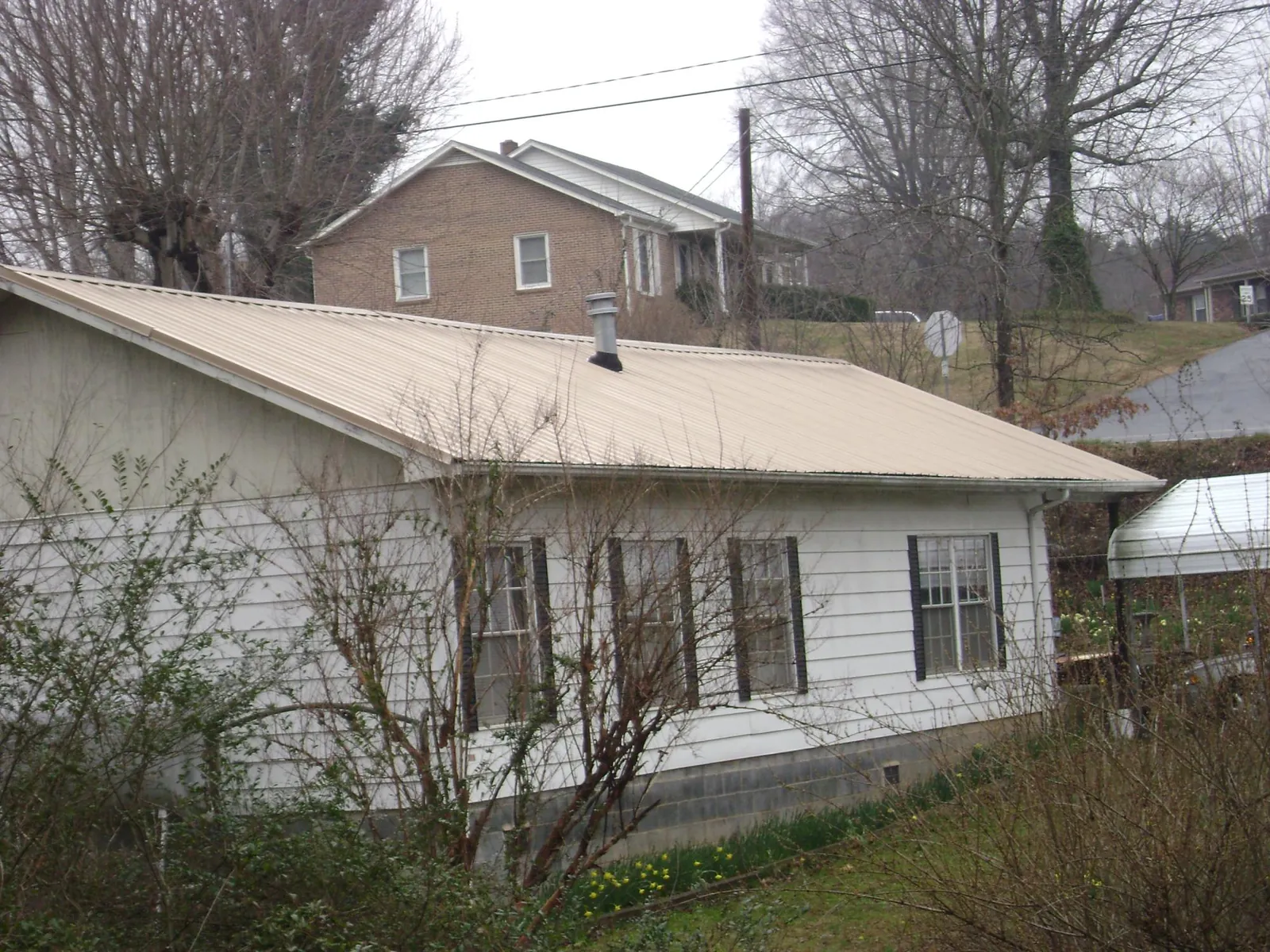 Tan metal roof on a white sided house set into a hillside — Commercial Roofing by Roofing Brothers in De Witt